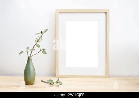 Empty wooden picture frame with passe-partout as mock-up and a vase with sage twig on a light table or desk in front of a white Stock Photo