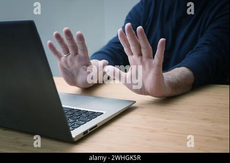 Hands in defensive gesture against a laptop computer, avoiding further work on a hacked system or other danger and offence, onli Stock Photo