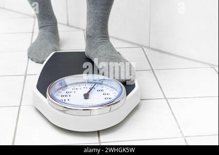 Feet in socks stepping on a personal scale on the tiled bathroom floor to measure the body weight, copy space Stock Photo