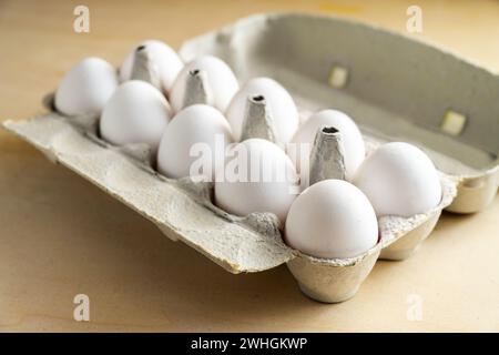 Ten fresh white eggs in a cardboard box on a wooden table, food and Easter concept, selected focus Stock Photo