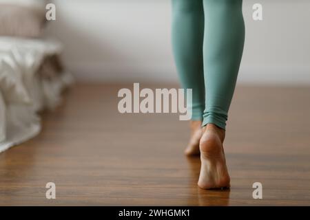 Young woman in sports leggings walks barefoot on the warm floor in the bedroom. Close-up of cropped image of barefoot girl. Unde Stock Photo