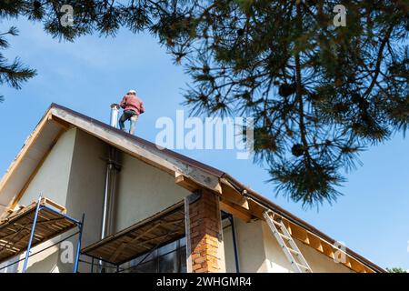 The master for the installation of ventilation pipes and the installation of the chimney of the furnace works on the roof of the Stock Photo