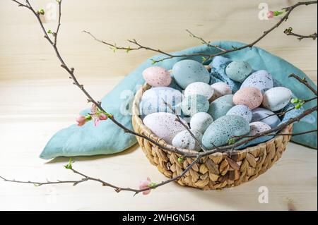 Many pastel colored Easter eggs in a basket and a branch with some flowers on a wooden table, copy space, selected focus Stock Photo