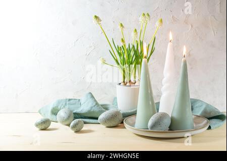Easter eggs and candles in pastel turquoise color and a potted white grape hyacinth on a wooden table against a light plastered Stock Photo