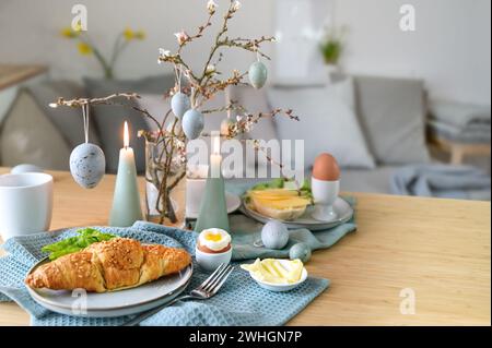 Breakfast table with boiled egg, croissant and pastel turquoise Easter decoration in a small living room, copy space, selected f Stock Photo