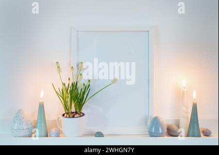 Decoration with an empty picture frame, candles and easter eggs in dusty blue green colors and a potted grape hyacinth plant on Stock Photo