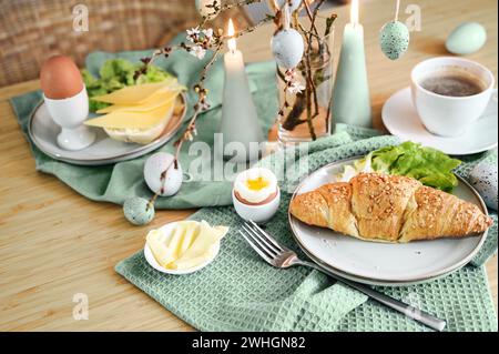 Breakfast with Easter eggs, croissant, coffee and sage green decoration with candles on a wooden table, copy space, selected foc Stock Photo