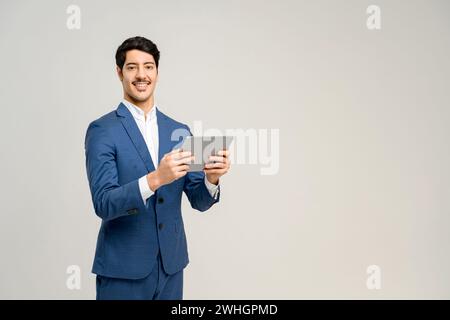 A man in a blue suit confidently uses a tablet, his smile conveying ease and expertise with technology, concept of business communications, digital solutions, and tech-facilitated business management Stock Photo