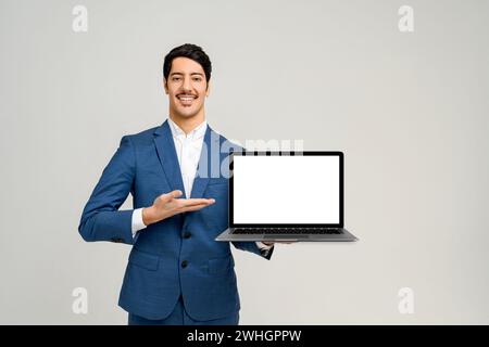 Man in a smart blue suit stands against a clean background, holding a laptop with a blank screen towards the camera, the perfect template for graphic designers to superimpose an application or website Stock Photo