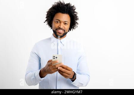Joyful and carefree African-American businessman using smartphone isolated on white, black guy spends leisure in social networks, chatting online, shopping, using new mobile app, playing game on phone Stock Photo
