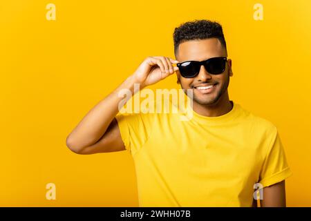 Handsome attractive young Indian guy in sunglasses posing isolated on yellow background. Carefree young masher man looking at camera and laughing, flirting with you Stock Photo