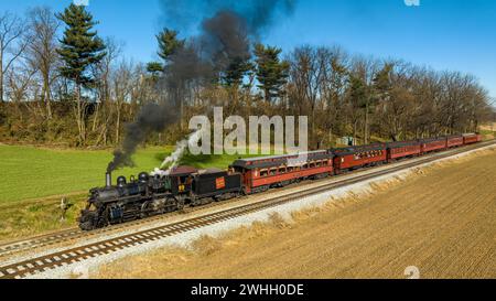 Drone View of a Restored Steam Passenger Train Traveling Thru Farmlands Pulling Up to Small Station Stock Photo