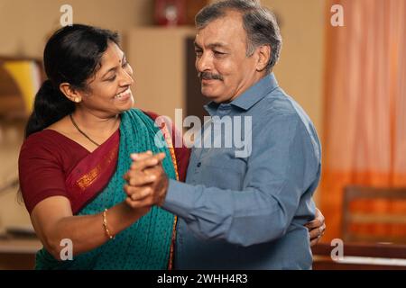 Happy Indian senior coupes dancing together by holding hands at home - concept of freedom, retirement lifestyle and entertainment Stock Photo