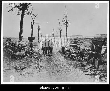 Summer 1918: German soldiers supporting an injured Canadian near Arras, in France, during World War I.  The destroyed vehicles and burnt trees framing the trio of men are, in contrast, a sharp reminder of war's destructiveness. Dates / between :26 August 1918-3 September 1918 Stock Photo