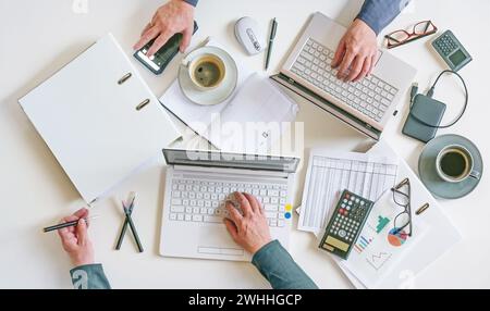 Top view of a white office desk with hands of two people working on laptops with papers, calculator, and coffee, teamwork and ac Stock Photo