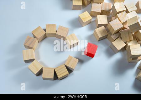 Many wooden cubes, some of them together forming a circle with a gap, one in red color is ready to complete the team, light blue Stock Photo