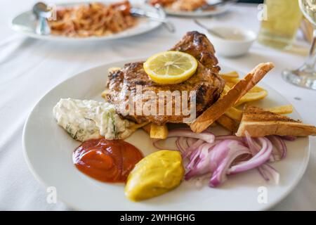 Roasted pork steak with French fries, onions, various dips and a lemon slice, barbecue dish in summer on a white plate, selected Stock Photo