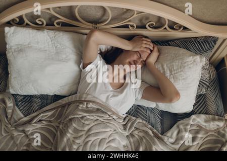 Young woman with headache flu ill sick disease cold at home indoor lying on bed. Stock Photo
