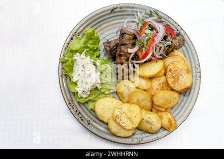 Mediterranean minced meat rolls with fried potato slices, salad and dip on a plate, white table, high angle view from above, cop Stock Photo
