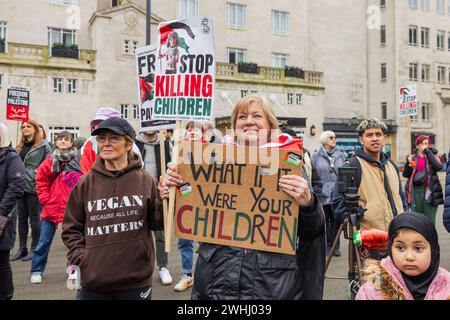 Leeds, UK. 10 FEB, 2024.  Smiling demonstrator holds 'What if it were your children' sign in city square in Leeds. Credit Milo Chandler/Alamy Live News Stock Photo