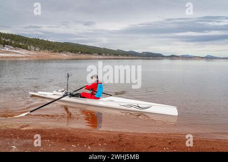 Loveland, CO, USA - February 6, 2024: Senior rower is landing Liteboat rowing shell on a shore of Carter Lake in northern Colorado in winter scenery. Stock Photo