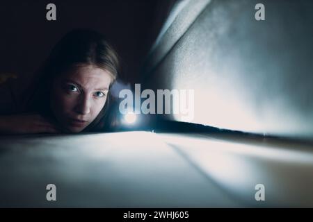 Woman young holding hand flashlight looking for dirt under furniture. Stock Photo