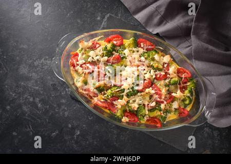 Casserole from broccoli, tomatoes, onions, feta and cheese, healthy vegetable dish on a dark gray slate background, high angle v Stock Photo