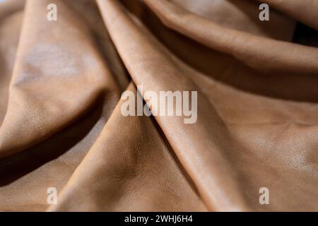Soft brown leather laying in waves, used for furniture, bags or clothing in a craft workshop, full frame background, copy space, Stock Photo