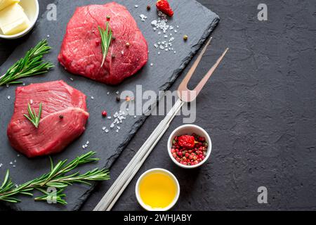 Raw meat beef steaks on black slate board, spices and ingredient Stock Photo