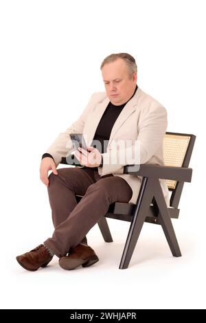 man in a chair watching something on his phone on a white background Stock Photo