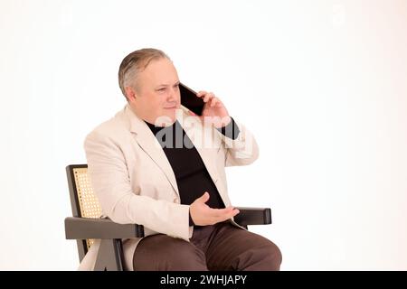 man sitting in a chair and talking on the phone on a white background Stock Photo
