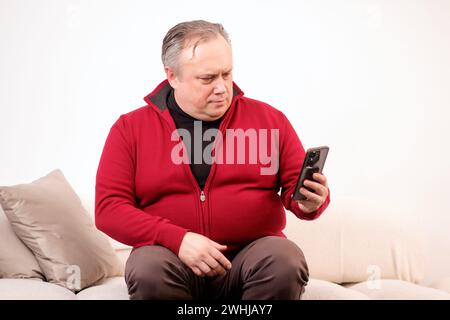 man talking or watching something on his phone while sitting on the sofa Stock Photo