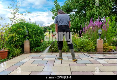 Cleaning stone slabs on patio with the high-pressure cleaner. Person worker in rubber boots cleaning Stock Photo