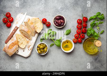 Food composition with sliced ciabatta, olives, olive oil, spaghetti, fresh basil, cherry tomatoes on gray concrete stone rustic Stock Photo