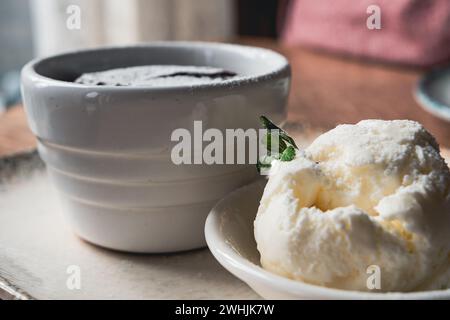 Molten chocolate lava cake and a scoop of ice cream served in ceramic jars, on a white plate with a silver spoon, on the wooden table, close-up shot. Stock Photo