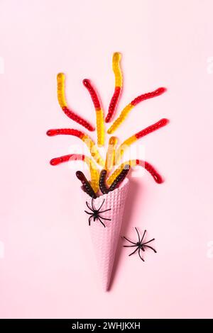 Pink ice cream cone with colorful marmalade worms and spiders. Minimal halloween composition Stock Photo