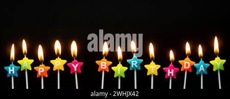 Burning candles with the words Happy Birthday, candles burning in long row, isolated on dark black b Stock Photo