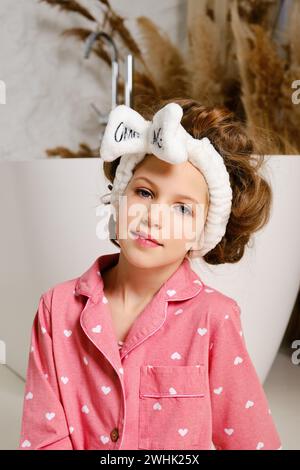 Portrait of nine years old girl in pink pajamas and a hairband that supports thick long hair Stock Photo
