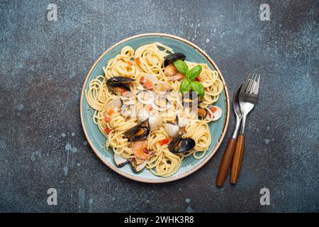 Italian seafood pasta spaghetti with mussels, shrimps, clams in tomato sauce with green basil on plate on rustic blue concrete b Stock Photo