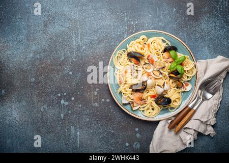 Italian seafood pasta spaghetti with mussels, shrimps, clams in tomato sauce with green basil on plate on rustic blue concrete b Stock Photo