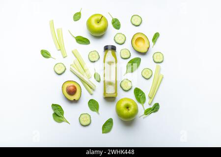 Bottle of green smoothie surrounded by green fruit and vegetables: apples, avocado, spinach, celery sticks, cucumber on white si Stock Photo