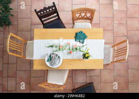 Preparation for a table setting with white plates and bowls, cutlery, green napkins and some tulip flowers, different wooden cha Stock Photo