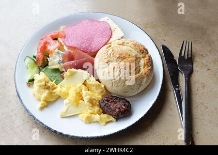 Breakfast plate with bread rolls, scrambled eggs, sausage, cheese and butter with cutlery on a stone table, selected focus Stock Photo