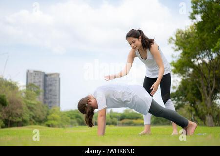 Young female and little girl with outdoor activities in the city park, Yoga is her chosen activity. Stock Photo