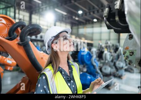 A female engineer installs a program on a robotics arm in a robot warehouse. And test the operation before sending the machine t Stock Photo
