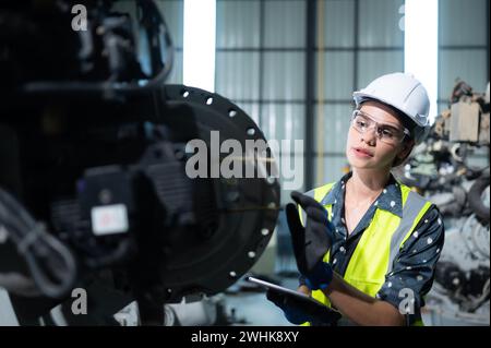 A female engineer installs a program on a robotics arm in a robot warehouse. And test the operation before sending the machine t Stock Photo