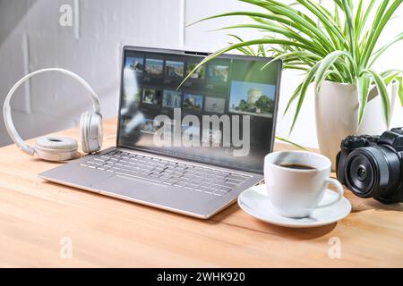 Desk from a media designer with laptop, camera and headphones, also a coffee cup and a plant on the wooden table against a white Stock Photo