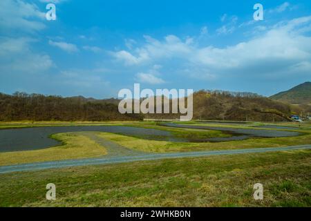 Landscape of ponds near rural mountain farming community under blue sky with puffy white clouds Stock Photo
