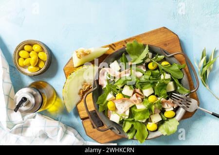 Summer mediterranean salad with melon, bacon, olives, white cheese and arugula on blue stone background. Traditional Spanish and Stock Photo