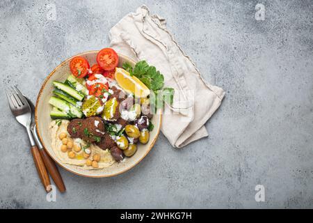 Falafel salad bowl with hummus, vegetables, olives, herbs and yogurt sauce. Vegan lunch plate top view on rustic stone backgroun Stock Photo